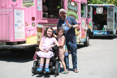 A father and two daughters, one in a wheelchair, pose in front of a dessert truck at FestAbility
