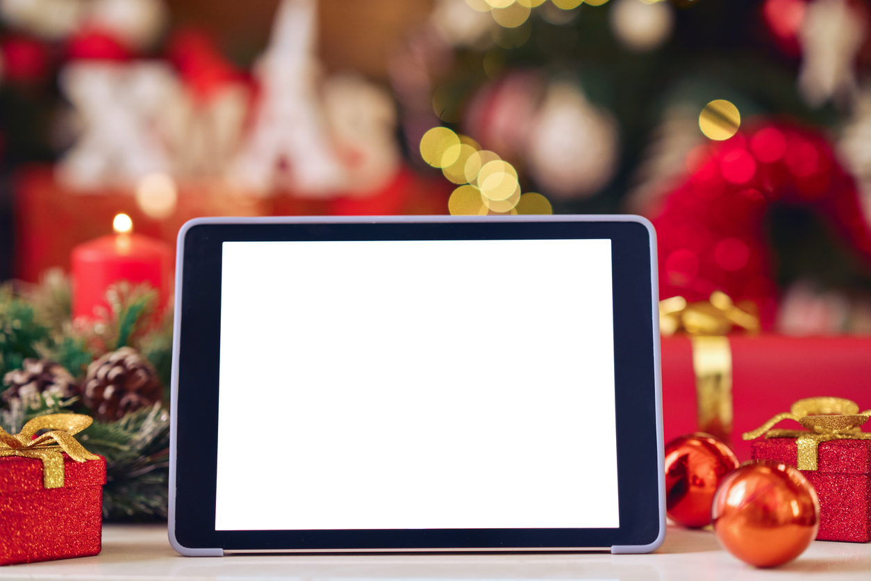 Digital tablet mockup white blank screen for ads on Christmas table holiday background. Xmas shopping online stores e commerce websites, virtual family party Happy New Year video calls concept.