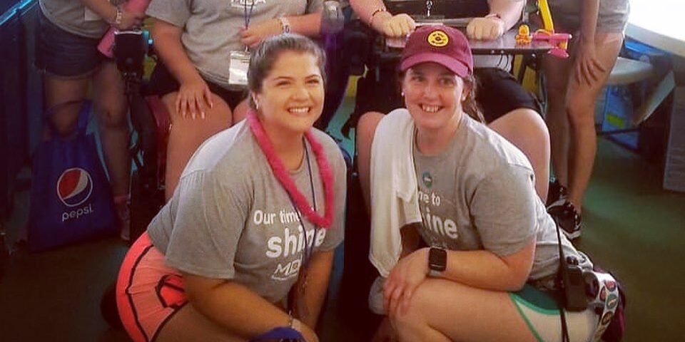 Two volunteer counselors in MDA T-shirts smile with a group behind them