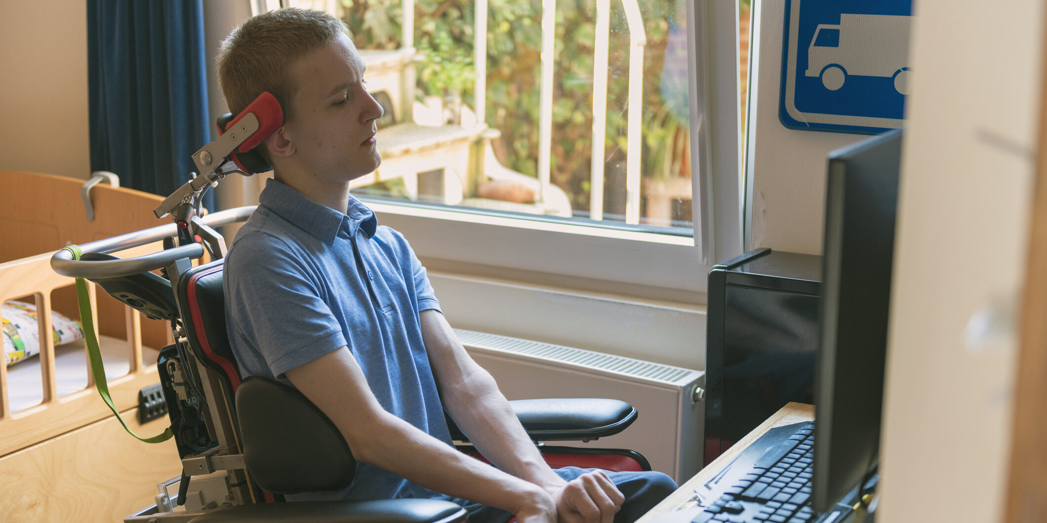 Color image of a real life young physically impaired ALS patient computer gaming with the help of his electronic wheelchair.