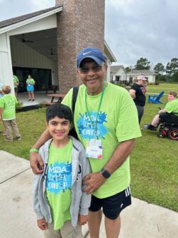 A grandfather and grandson pose outside a large building in matching lime green MDA shirts 