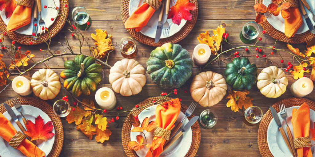 Autumnal decorated table for celebrating Thanksgiving or other family celebration. Festive table setting with plates, glassware, pumpkins, rose hip branches and leaves on wooden table background, top view