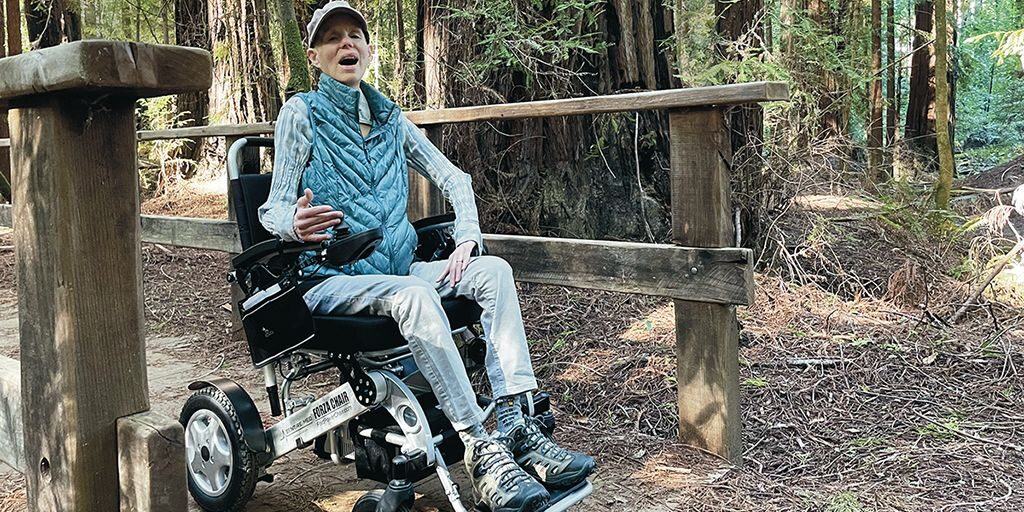 Leslie Krongold drives a power wheelchair on a boardwalk path through a redwood forest at Hendy Woods State Park.