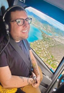Closeup of Cory Lee wearing headphones in a small aircraft with water and land visible outside the window.