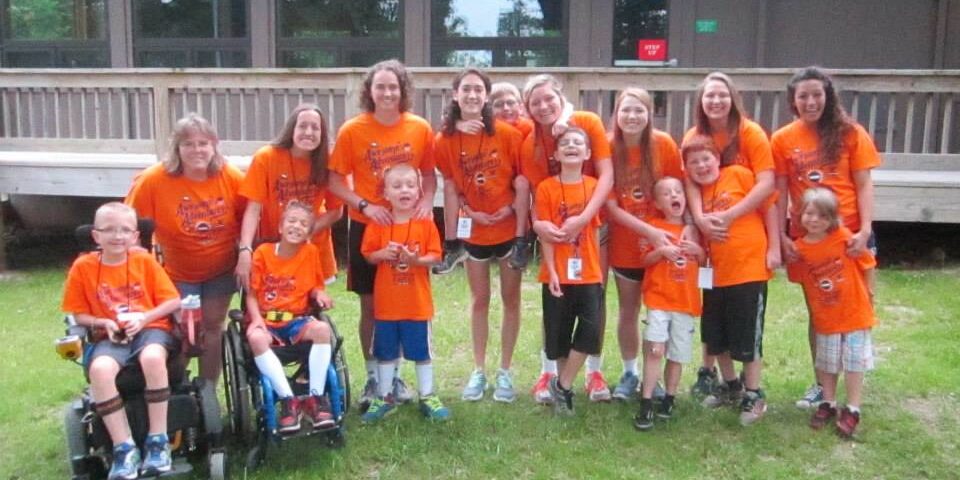 Campers, staff, and volunteers pose in matching orange MDA Summer Camp T-shirts