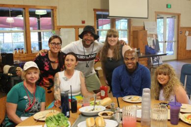 A group shot of MDA staff and volunteers at MDA Summer Camp gather around a dining hall table
