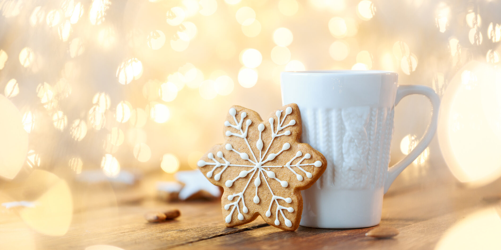 A beautiful white mug with a knitted print and a ginger cookie with icing in the shape of a snowflake on a background of garlands