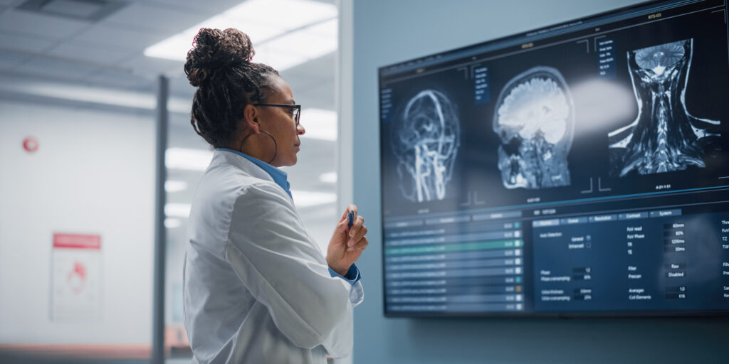 Medical Science Hospital: Confident Black Female Neurologist, Neuroscientist, Neurosurgeon, Looks at TV Screen with MRI Scan with Brain Images, Thinks about Sick Patient Treatment Method. Saving Lives