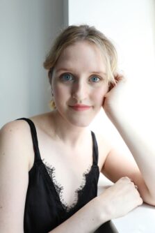 Emily Muller headshot, blonde woman resting her head on her hand and wearing a black tank top