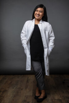 Dr. Dwi U. Kemaladewi wears a white lab coat and smiles in front of a grey backdrop