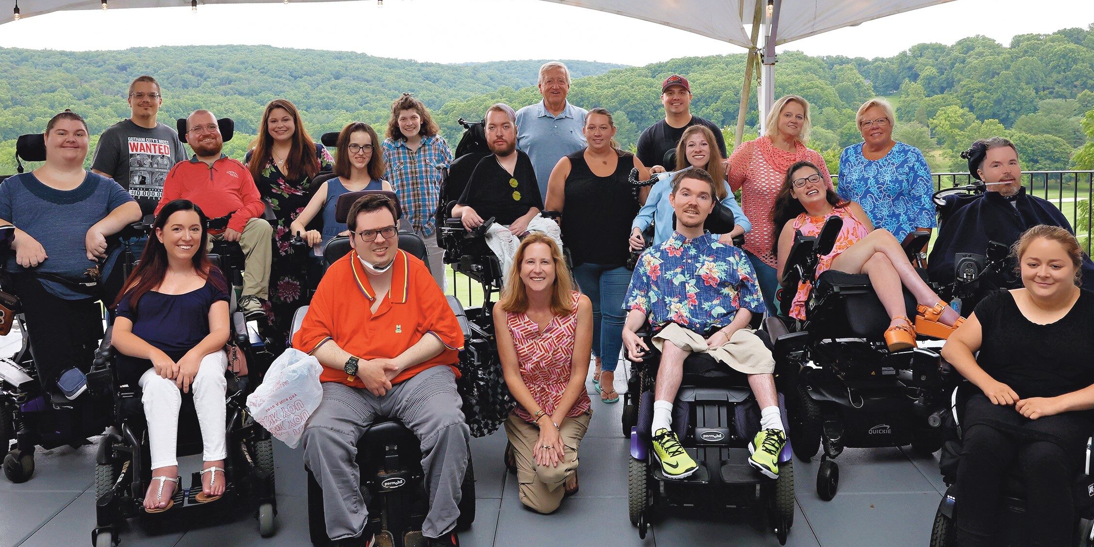 Twenty former MDA Summer Campers and counselors gather on a patio with a backdrop of green forested hills.
