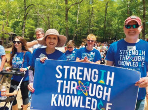 A group of walkers wear shirts and carry a sign with the phrase “Strength Through Knowledge.”