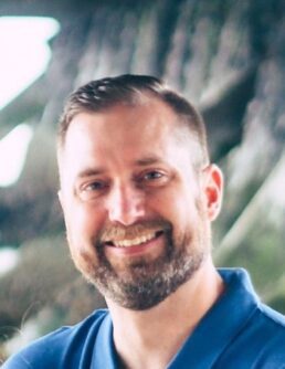 Headshot of Scott Wiebe, a while man with a beard smiling outside in a blue polo shirt