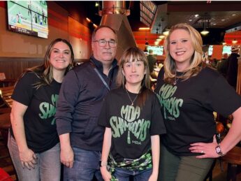 Three women in MDA Shamrock t-shirts pose with a man in a black pull over inside a pub