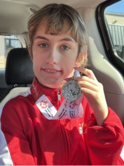 A young woman in a red athletic zip up holds a Special Olympics medal