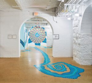 At the MuseumLab at the Children’s Museum of Pittsburgh, a mural of a flower-like red and orange circle on the wall in a hallway has bright blue tendrils that extend on the floor through arched doorways leading to other rooms.