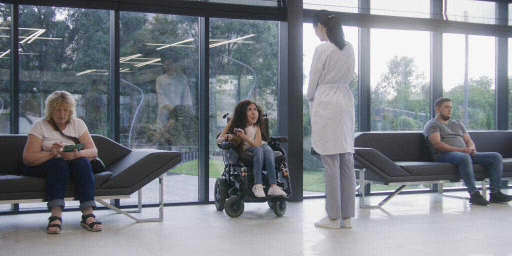 Woman in electric wheelchair waits for consultation with doctor in clinic waiting area. Nurse invites patient with disability on procedures. Medical staff and people in modern medical facility lobby.