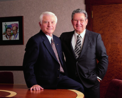 Two men stand in suit and ties inside of an office