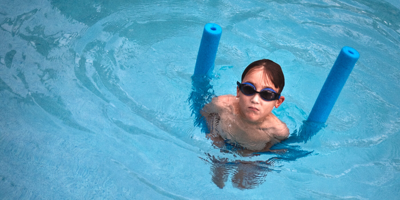 little kid with dark goggles in a swimming pool playing with a floating device