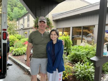 A man in green shirt poses with a young woman in a blue sweater outside