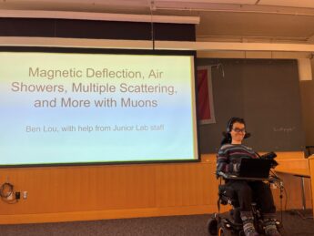 A young man in a power wheelchair presents in front of a classroom