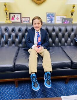 A young boy wearing a suit smiles on a leather couch