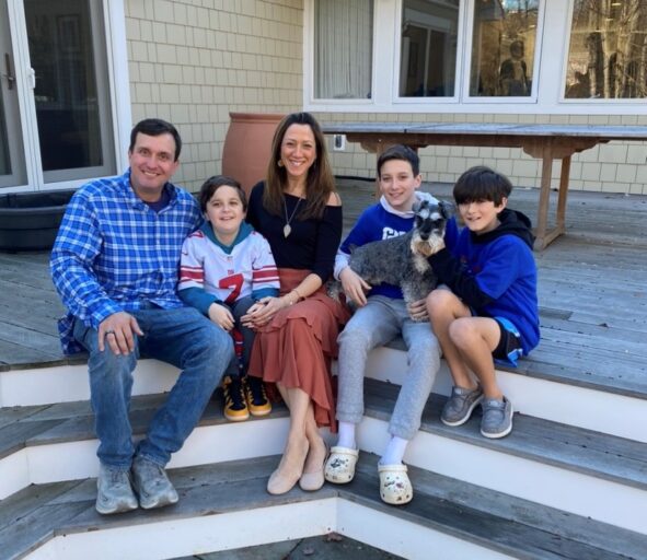 A father, mother, and three sons sit on an outdoor patio step