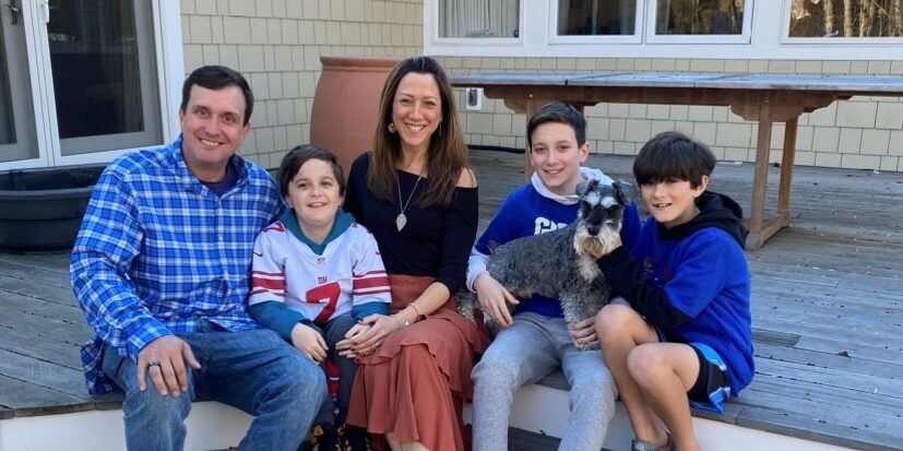 A father, mother, and three sons sit on an outdoor patio step