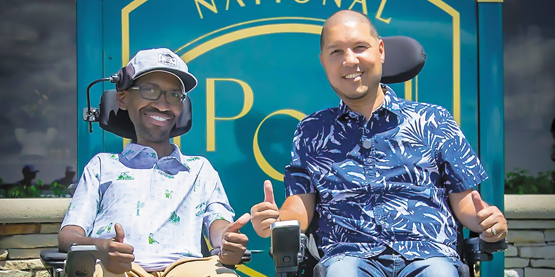 Two MDA Ambassadors sit side-by-side in power wheelchairs, smiling at the camera.