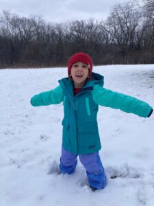 Four-year-old Kenzie Graves stands in the snow with arms stretched out, with a big smile on her face.