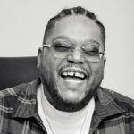 Black and white image of Fred Graves, a man with dark skin, hair in cornrows, a close-cut beard, and rimless glasses.