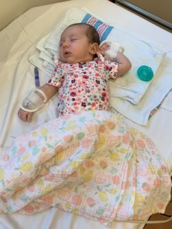 A newborn baby sleeping in a pink onesie with a hospital bracelet on