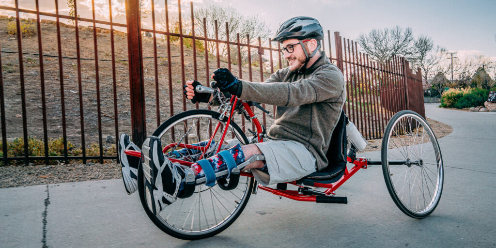 Handsome Young Man with Myelomeningocele Spina Bifida Riding a Red Handcycle Wearing Orthotic Leg Braces for Adaptive Exercise Outdoors in the Spring. Overcoming the Stigma and Challenges of Disability can be Fun on a Hand bike!