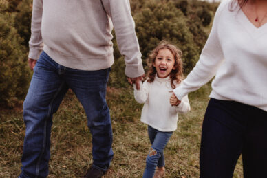 A young girl walks through a field holding hands with her parents