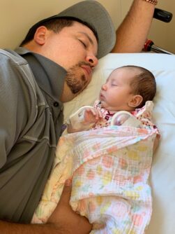 A dad sleeps next to his sleeping infant on a hospital bed