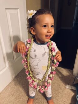 A toddler stands with flowery necklaces on