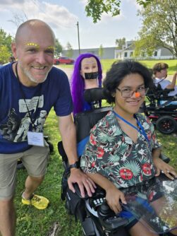 A man and young person in a wheelchair wear silly makeup and smile at the camera