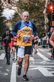 A man in an MDA jersey runs on the street in the NYC marathon