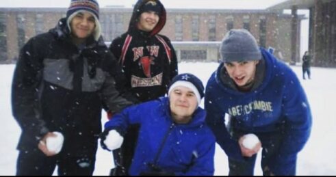 Four college students holding snow balls outside of dorm buildings.