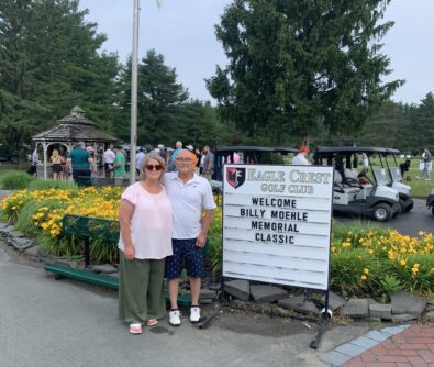 A woman and man stand in front of a sign that reads "Welcome Billy Moehle Memorial Classic"