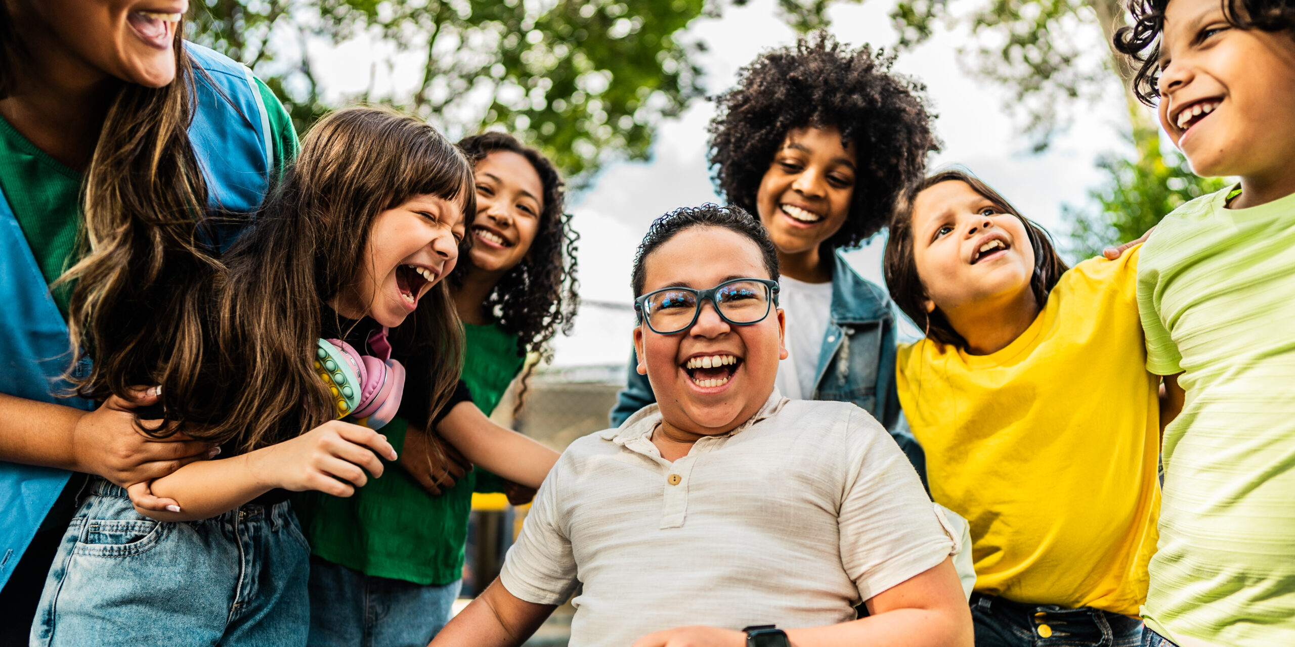 A group of young children of different ethnicities and disability laugh together.