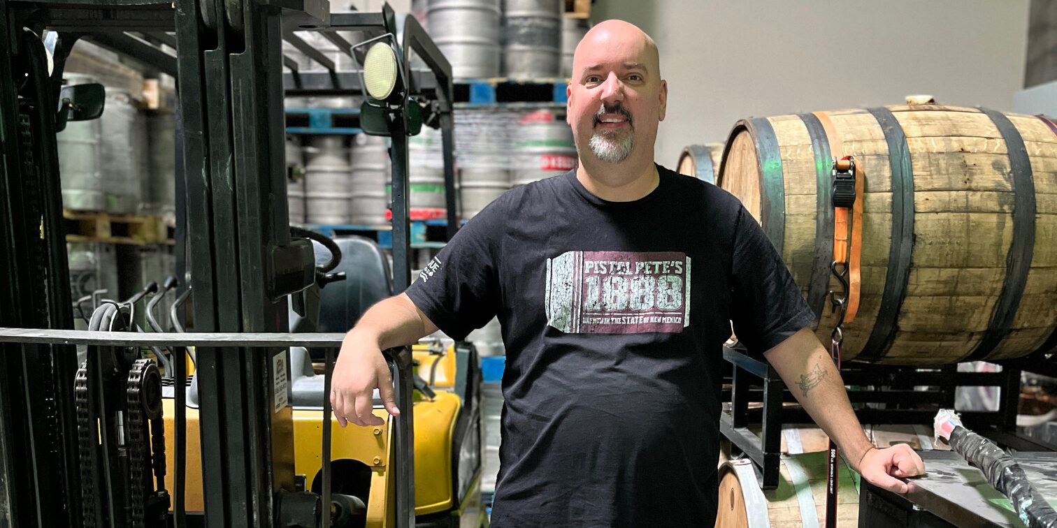 Scott Conger stands in front of barrels and machinery at a brewery.