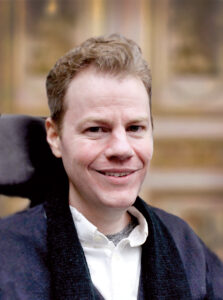 A close-up profile of Richard Vagen, who is wearing a white-collared shirt and blue blazer and smiling at the camera.