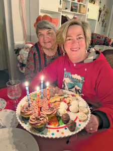 Therese Gabriel and a guest sit at a holiday dinner table with a platter of dessert cookies and cupcakes in front of them.