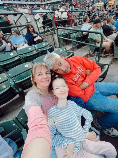 Three people take a selfi at a large stadium