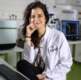 A woman scientist in a white lab coat with long brown hair 