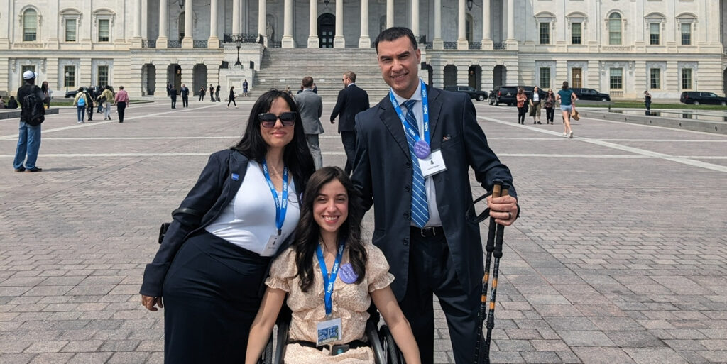 A young woman in a wheelchair poses with her parents in front of the Capitol