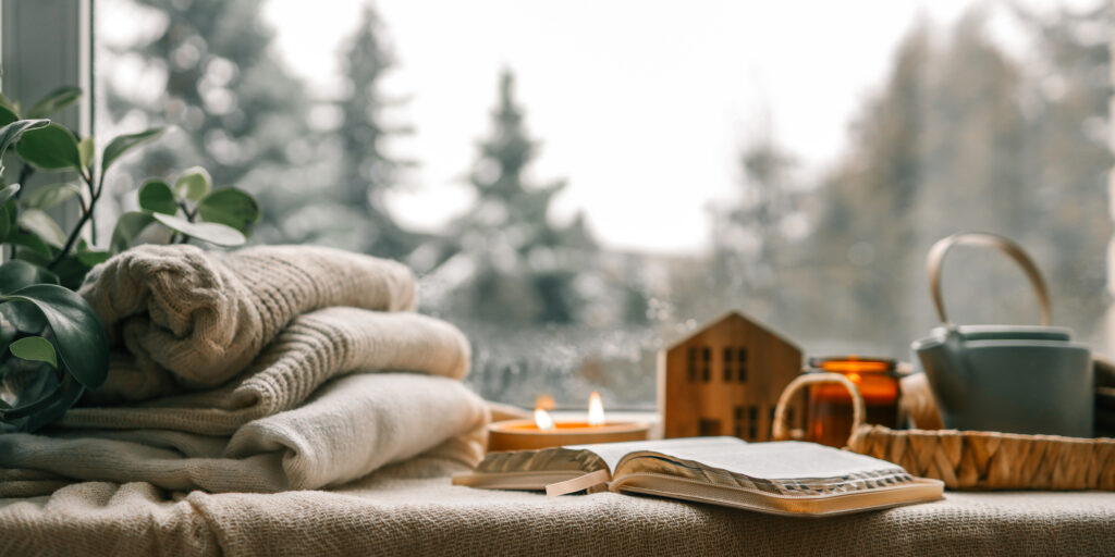 Cozy winter photo, stack of sweaters, open book, tea and candle.