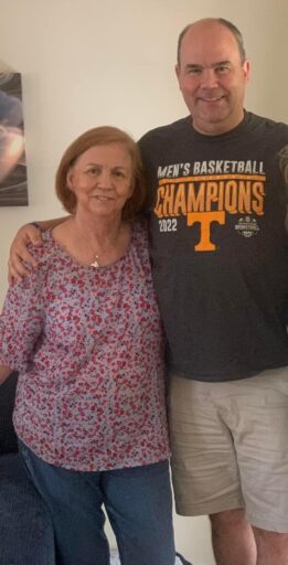 A woman in a flowered shirt smiles with her arm around a taller man in a Tennessee t-shirt