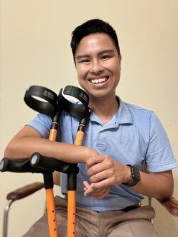 A young man with black hair wearing a light blue polo shirt holds a pair adaptive canes